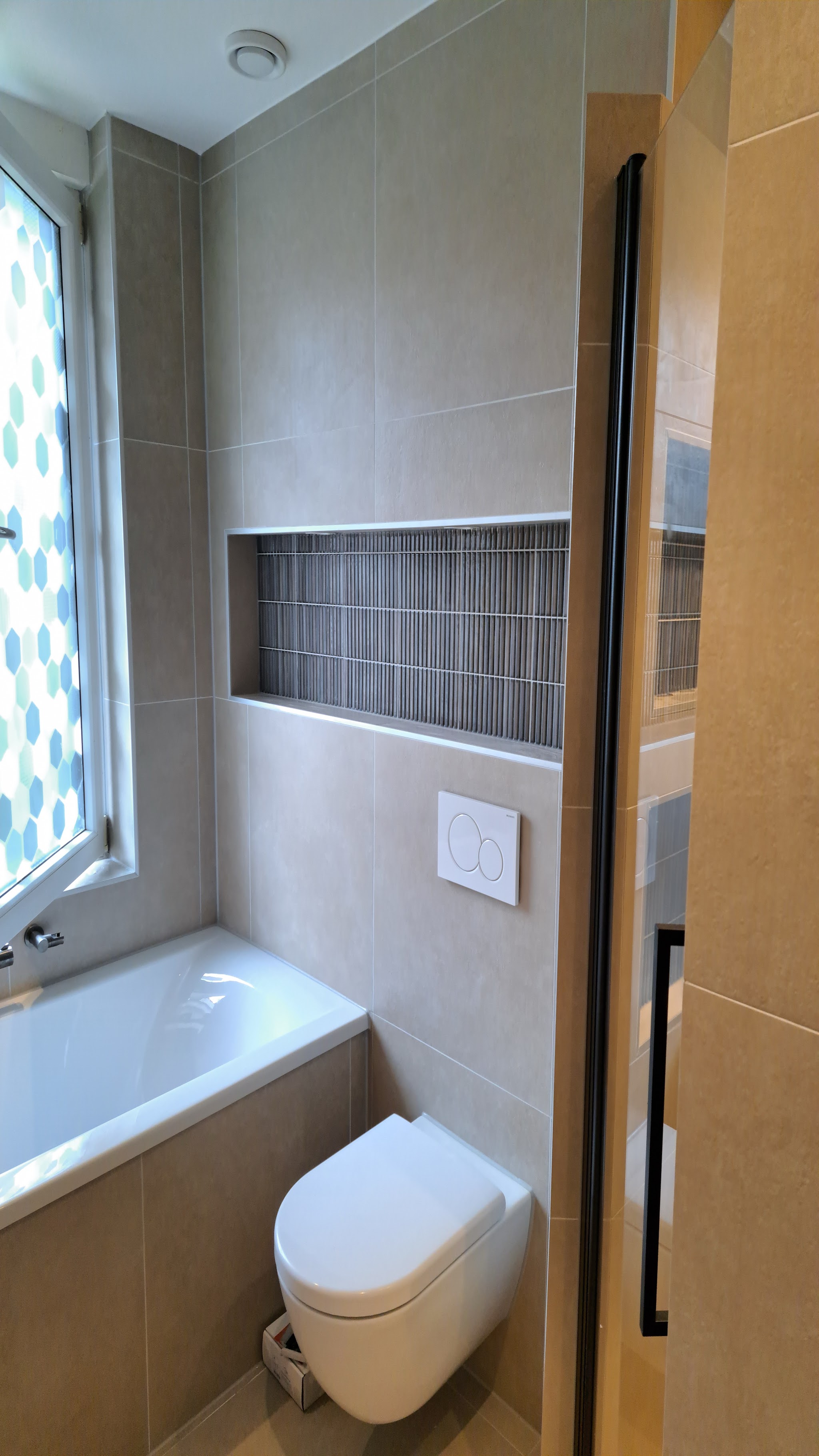 Badkamer met ligbad, beige tegels en een mozaïek nis