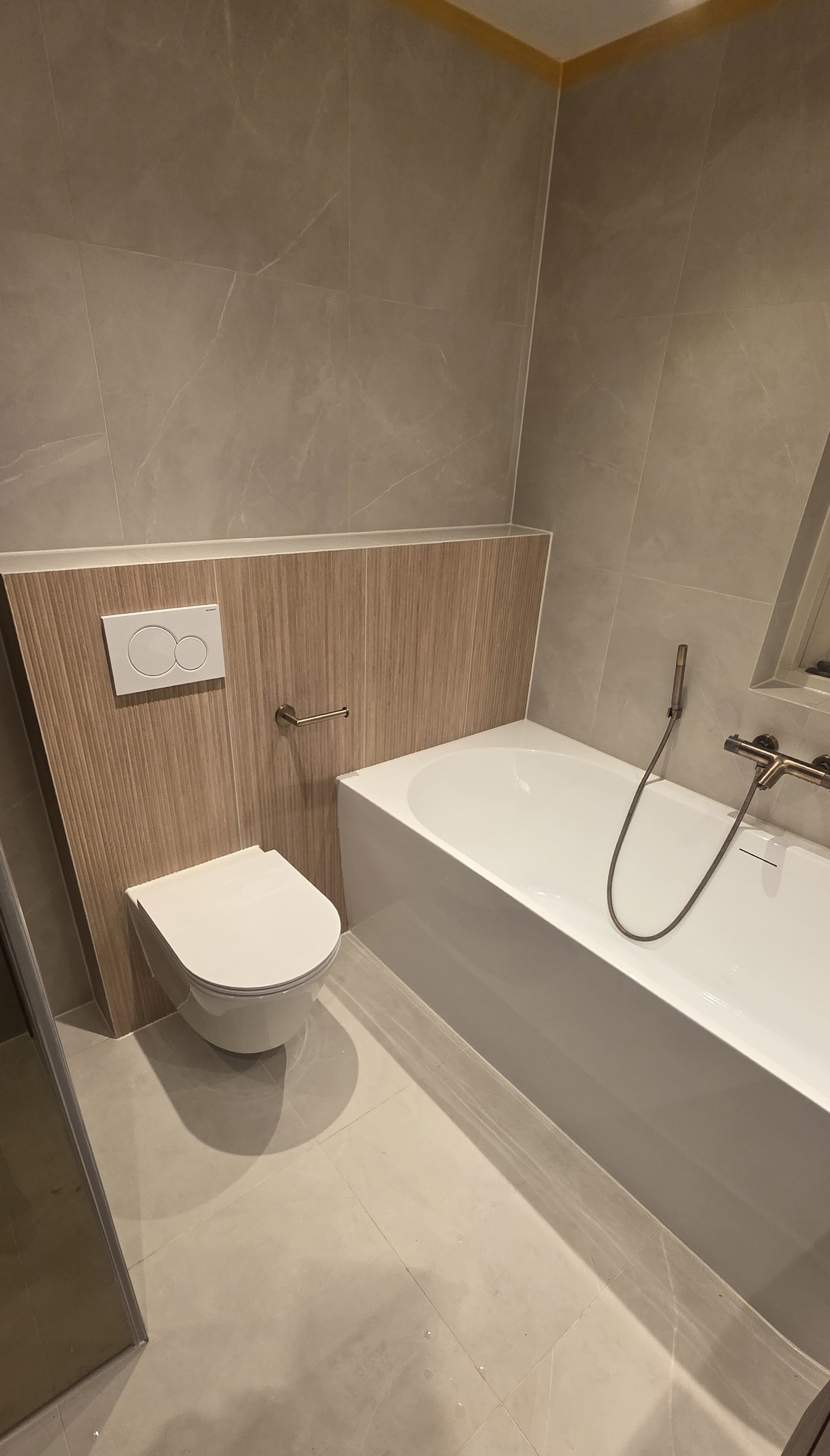 Badkamer met marmerlook tegels, ligbad en geborsteld bronzen kranen